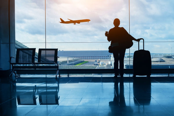 Pessoa com mala em um aeroporto esperando para embarcar em um avião, uma alusão à imigração.